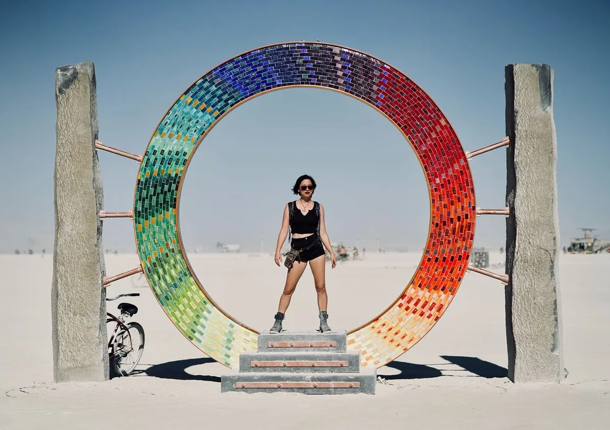 A person stands centered inside a large rainbow mosaic ring on the playa