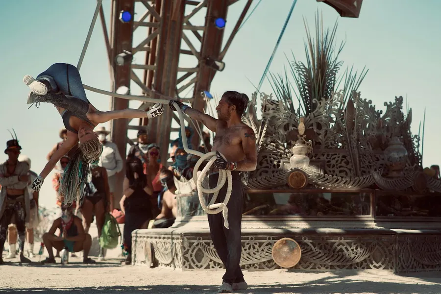 A shirtless performer holds several white hoops in front of an ornate mutant vehicle