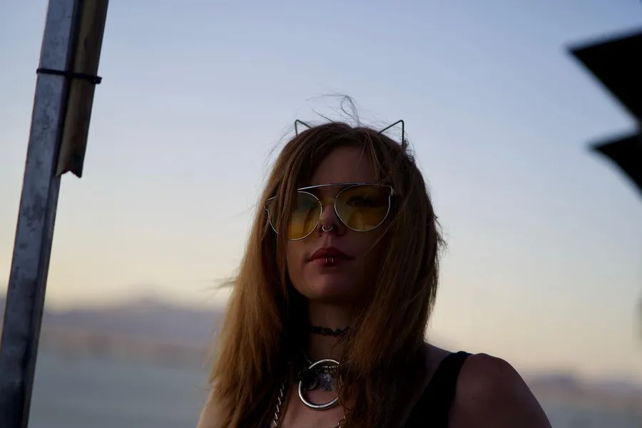 Close-up of a long-haired person wearing yellow glasses at dusk