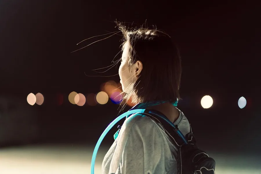 Side profile of a person wearing a backpack and glowing blue hoop at night