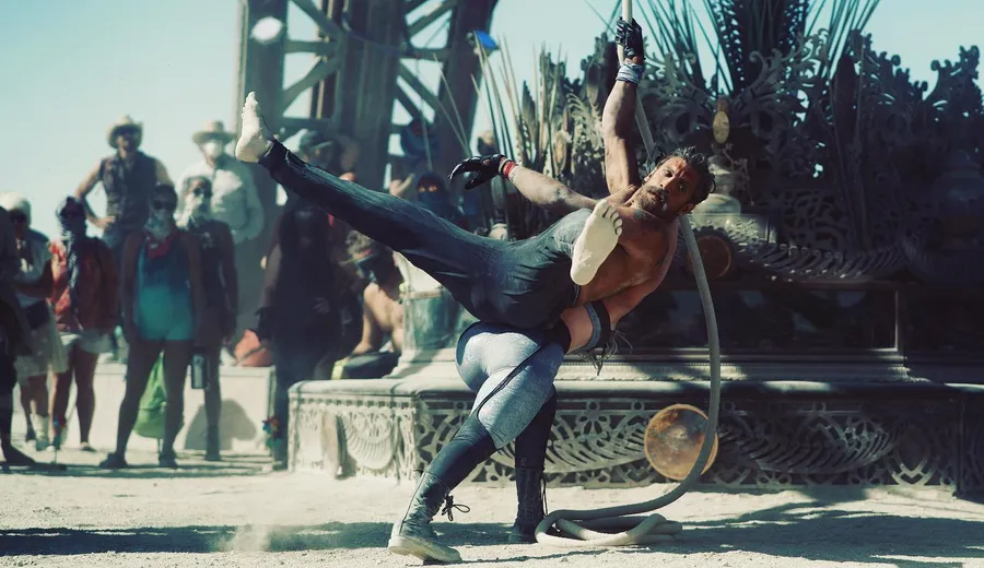 Two acrobats balance together with a large hoop in front of an ornate mutant vehicle