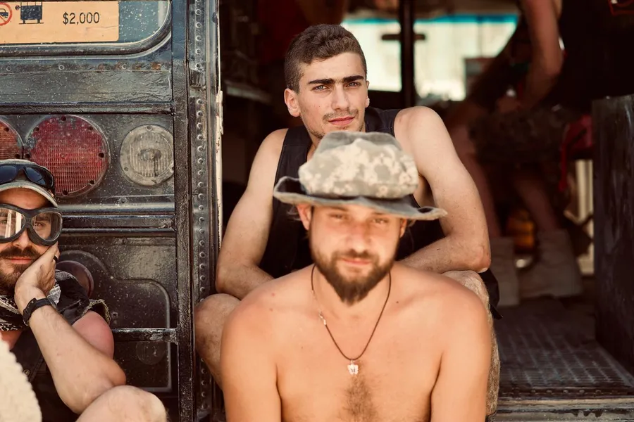 Three people sit together in the open doorway of a weathered vehicle