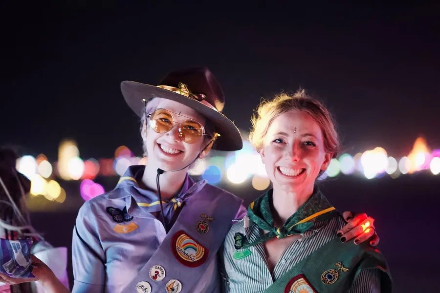 Two smiling people in patch-covered scout uniforms pose together at night