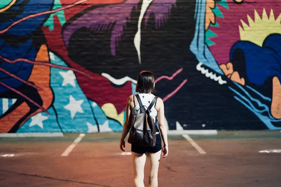 A person with a backpack stands facing a large colorful mural