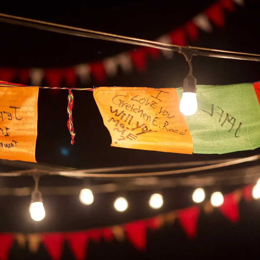 A proposal reading “Love you Gretchen, will you marry me?” hangs among handwritten flags and bare bulbs