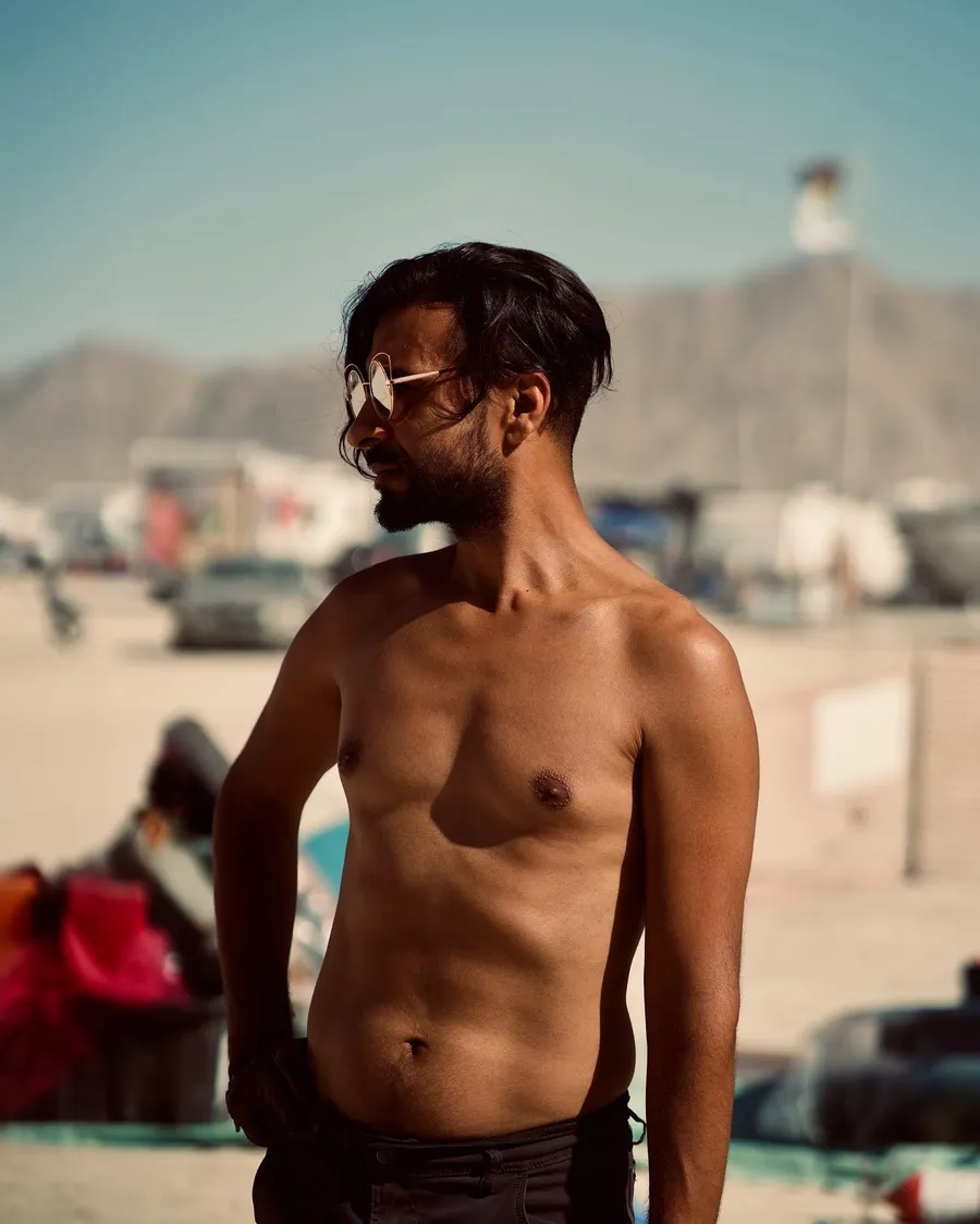 A shirtless man in round mirrored sunglasses stands on the playa