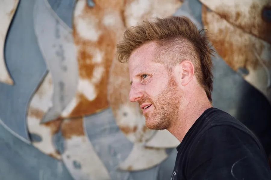 Side-profile portrait of a red-haired, bearded man against weathered metal