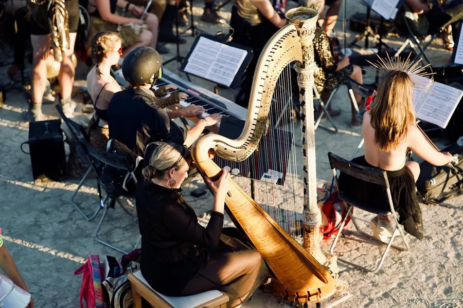 A harpist plays among an outdoor orchestra, seen from above