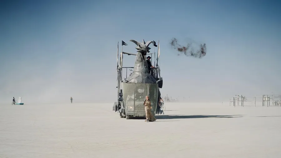 A tall silver horned mutant vehicle crosses the playa, trailing a ring of dark smoke