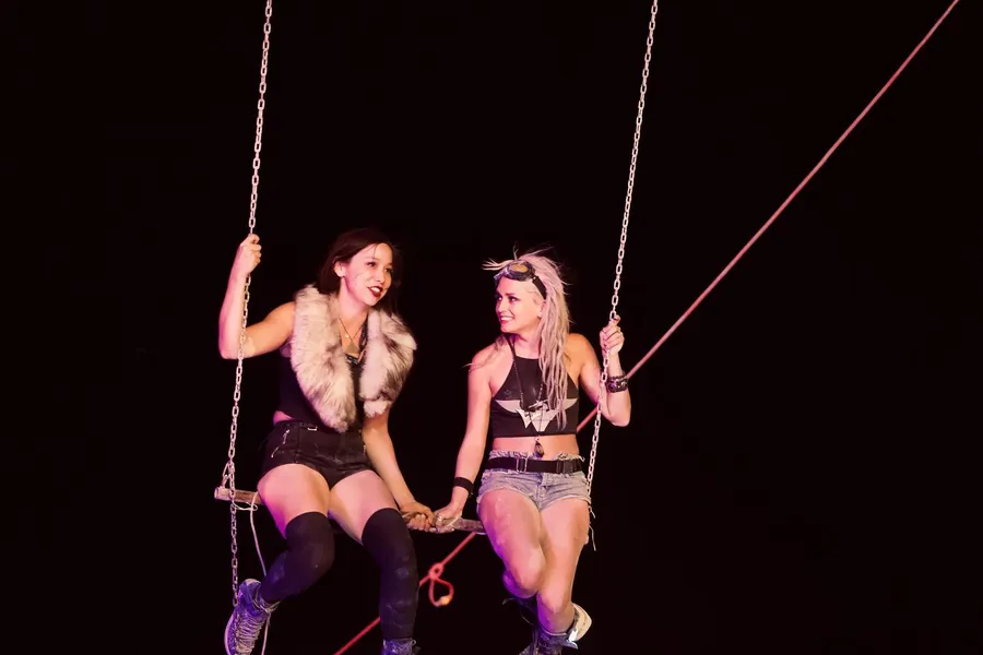 Two women sit together on a chain swing, holding hands in the night