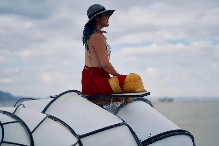 A person in red pants and a wide-brimmed hat sits atop a white segmented art vehicle