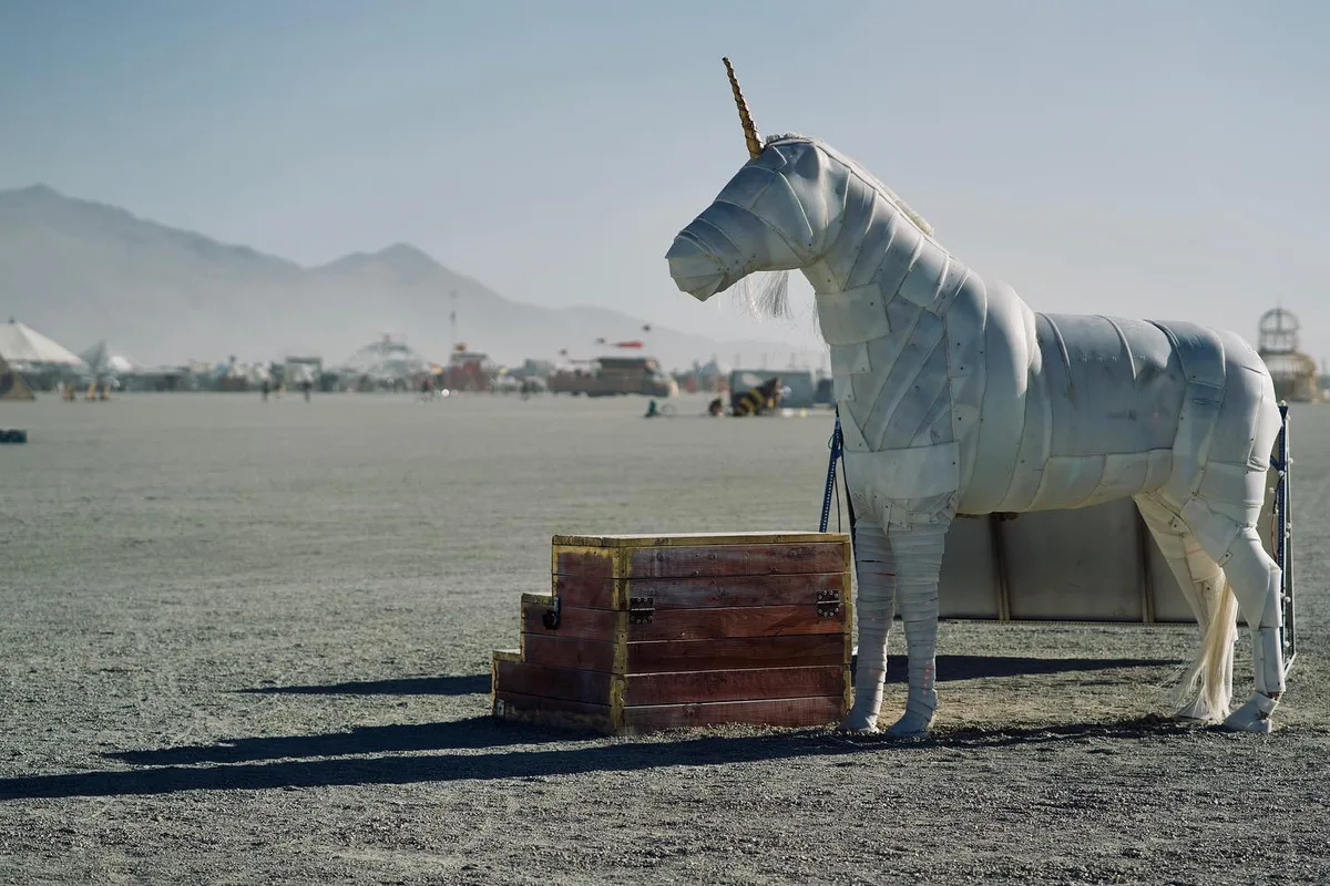 A life-size white unicorn sculpture stands beside wooden steps on the playa