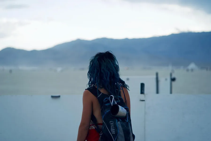 A person with a backpack seen from behind, looking across the playa toward distant mountains