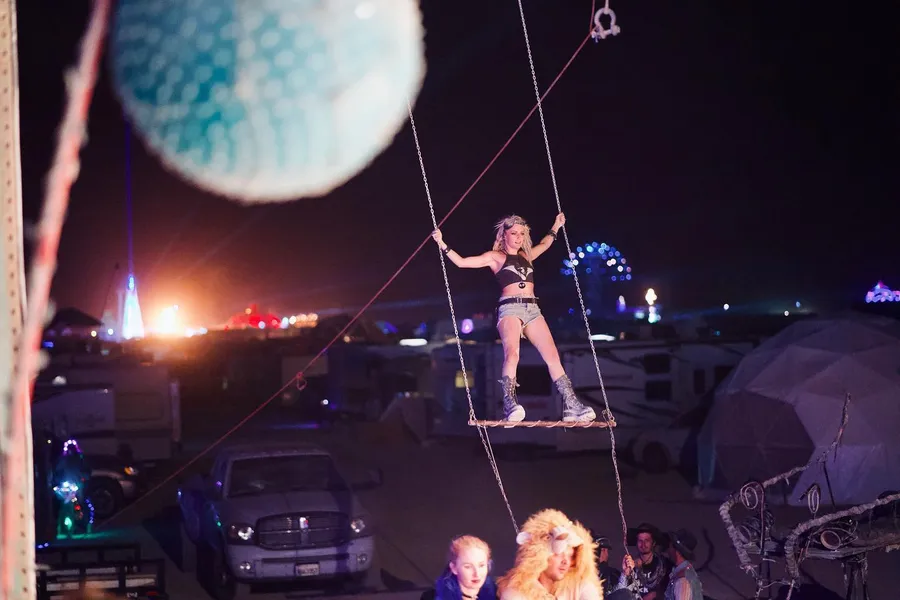 A woman balances on a suspended swing above a camp at night