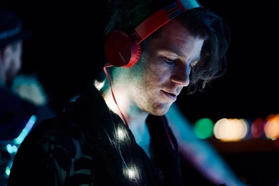 A man wearing red headphones looks down while surrounded by colored lights
