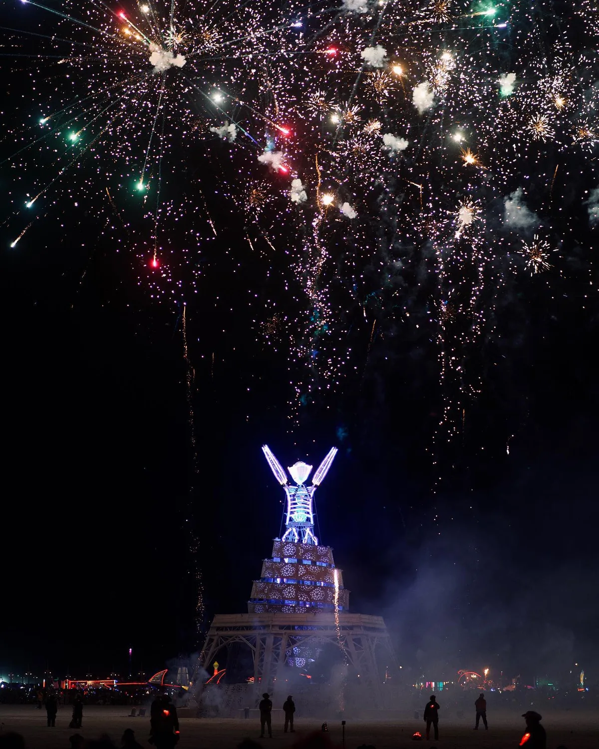 Fireworks burst above the illuminated Man sculpture at night