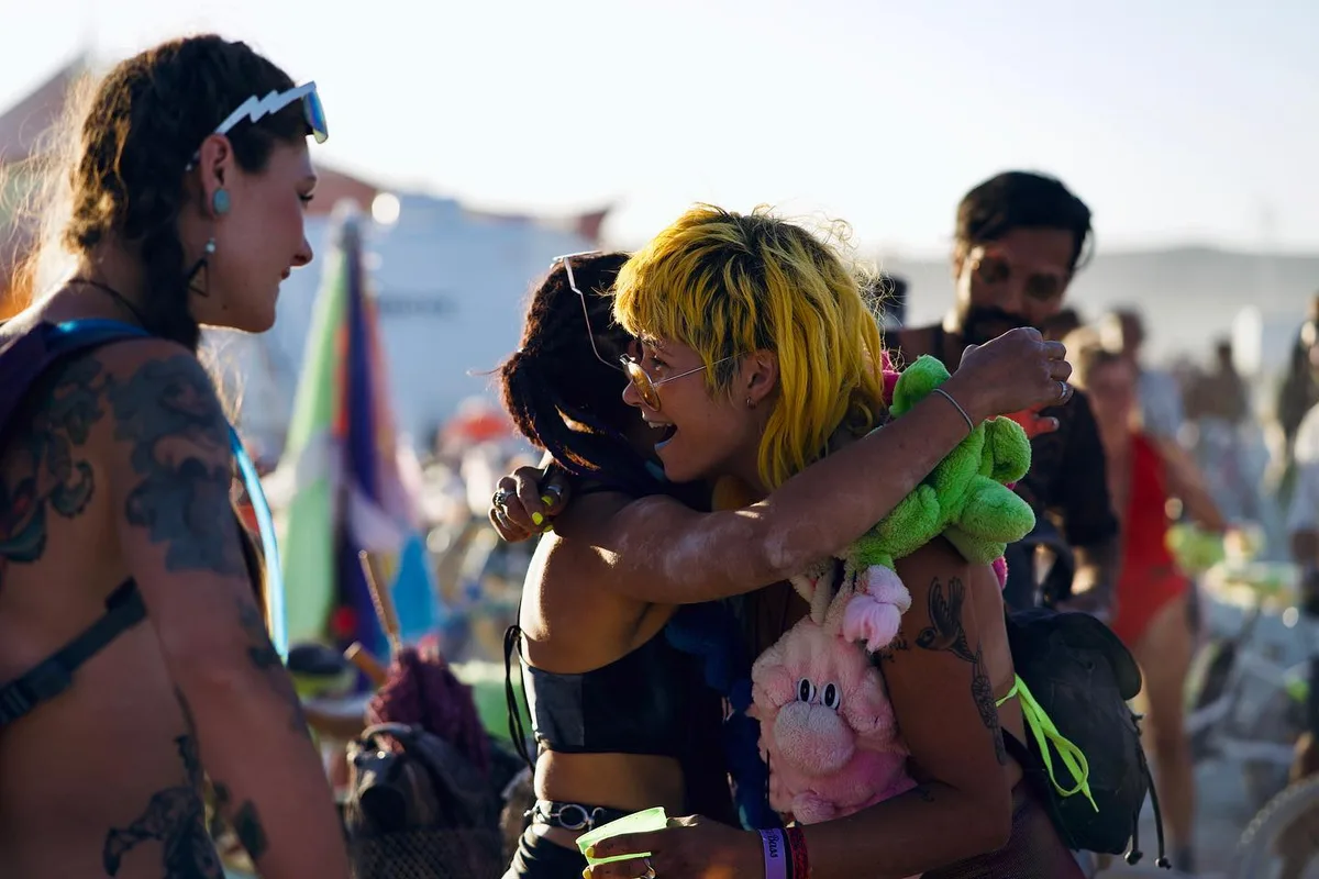 Two costumed people embrace in a daytime crowd, one with bright yellow hair