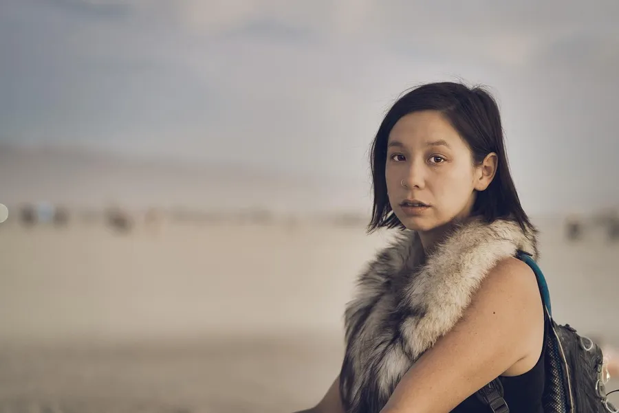 A woman wearing a fur collar looks toward the camera on the playa