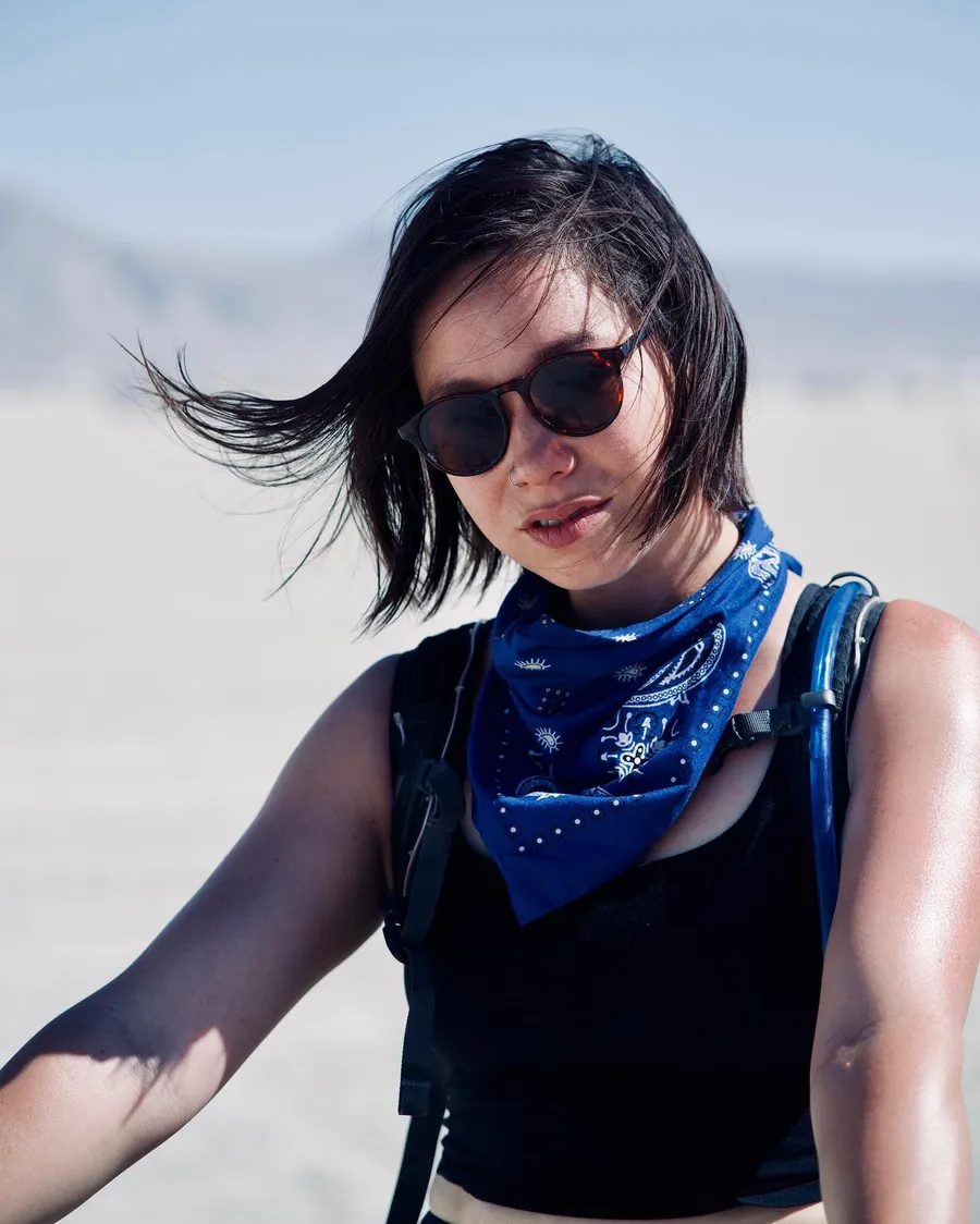 A woman in round sunglasses and a blue bandana looks down on the playa