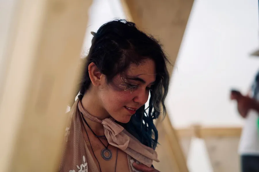 A woman looks down inside a beige tent with one hand resting on her chest