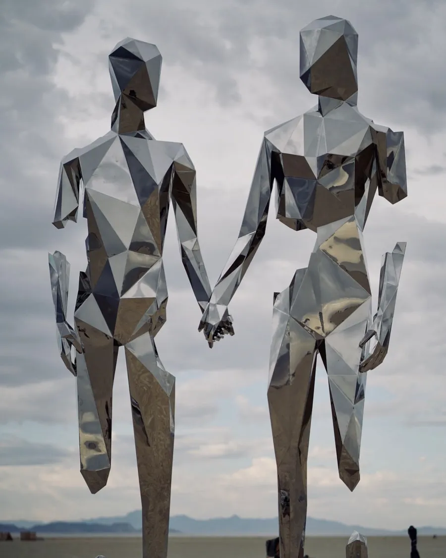 Two tall faceted metal human figures hold hands beneath a cloudy sky