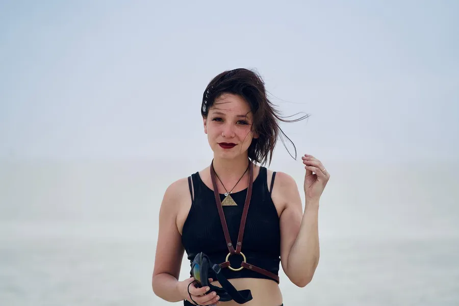 A woman holding a camera stands against the pale playa and sky