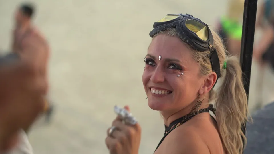 A smiling woman with goggles on her head and gems around her eyes at Burning Man