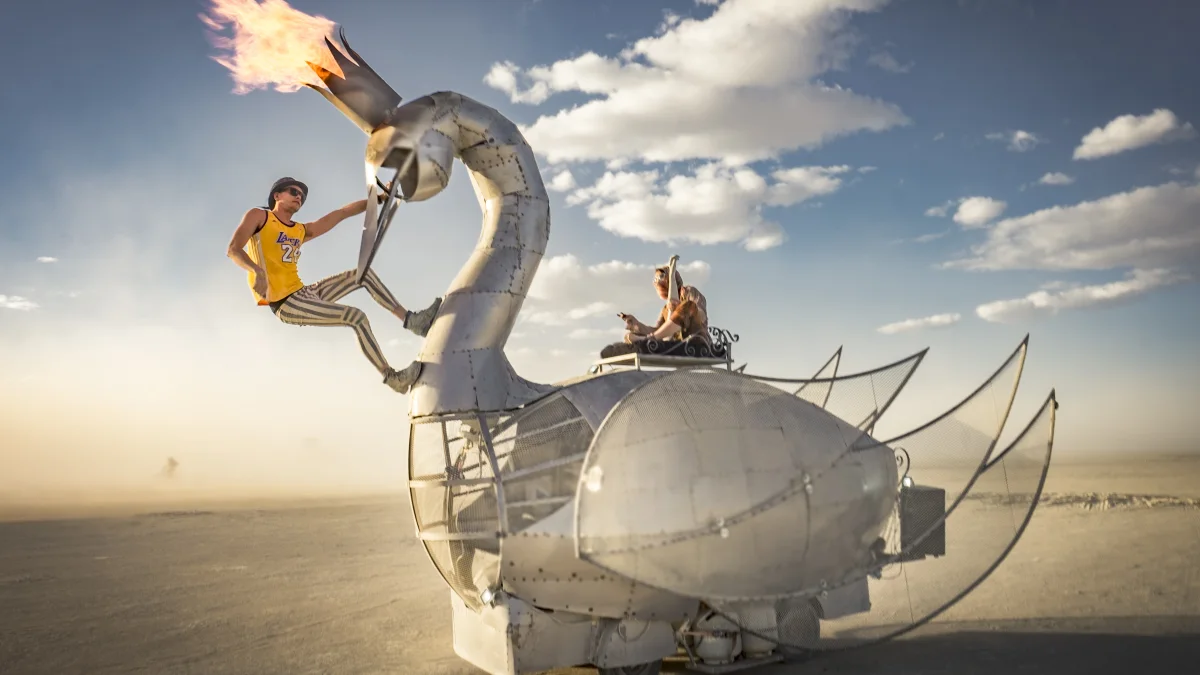The Prodigal Swan on the playa with its crown aflame, one rider seated and another hanging from its neck